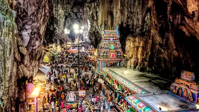 Inside a vast limestone cave, crowds stand around a brightly painted shrine lit by lamps