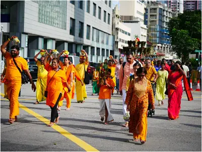 Men and women in orange and yellow walk in a procession along a city road