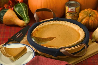 A pumpkin pie with a slice cut out, with pumpkins and autumn leaves behind