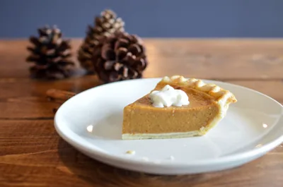 A slice of pumpkin pie with cream beside pine cones