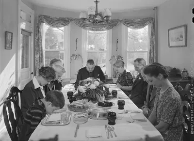 A black and white photo of a family saying grace at a dinner table