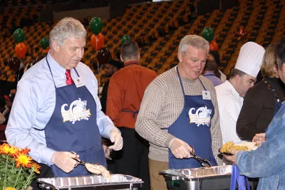 Volunteers in aprons serving food from large trays