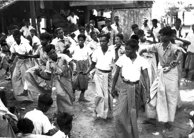 Old black and white photo of people in longyi dancing in a village street