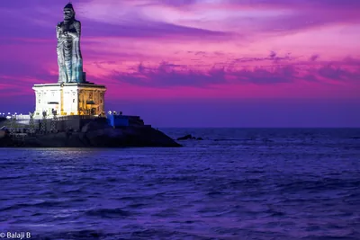 A tall stone statue on a rock island against a purple evening sky