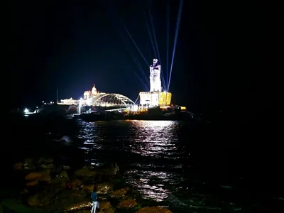 The statue lit with lights and beams at night, reflected in the sea