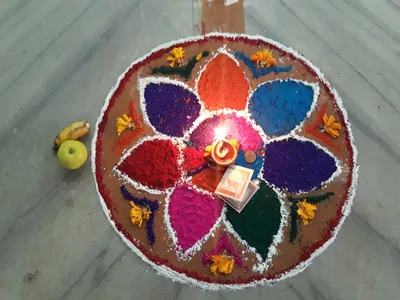 A colourful rangoli flower of coloured powder with a small lamp at its centre