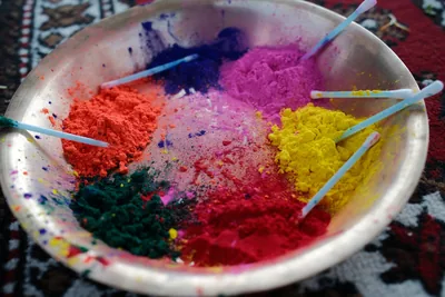 A metal bowl filled with heaps of red, yellow, pink and green coloured powder