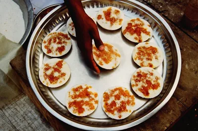 A steel plate of round rice pitha topped with jaggery and coconut