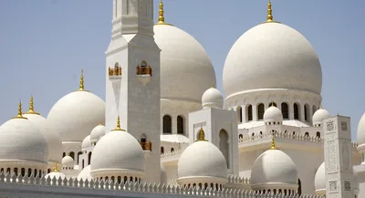 White marble domes and a minaret with golden tops under a clear sky