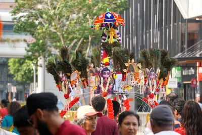 Devotees carrying tall kavadi decorated with peacock feathers down a street