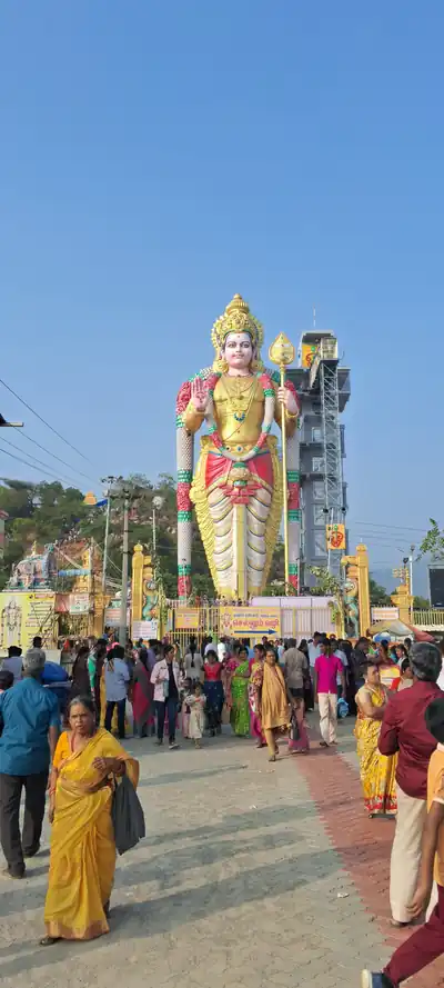 A giant colourful Murugan statue above a crowd at a temple
