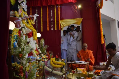 A puja hall with an image of Saraswati and people in white offering prayers