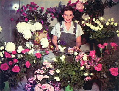 A woman behind a stall full of colourful flower garlands