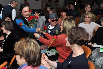 Women in a hall receiving red roses from colleagues on Women's Day