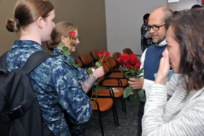 A woman in uniform smiles as she is given a red rose