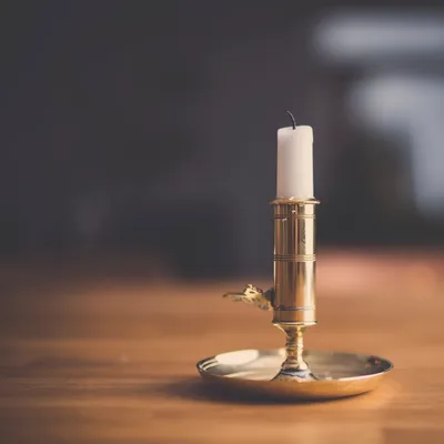 A single white candle in a brass holder on a wooden table