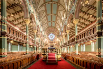 The grand interior of a synagogue with red carpet and painted arches